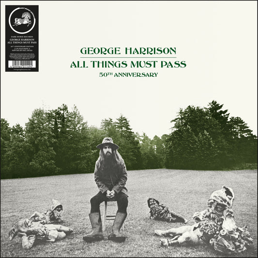 George Harrison sitting on a stool surrounded by garden gnomes in a grassy field.