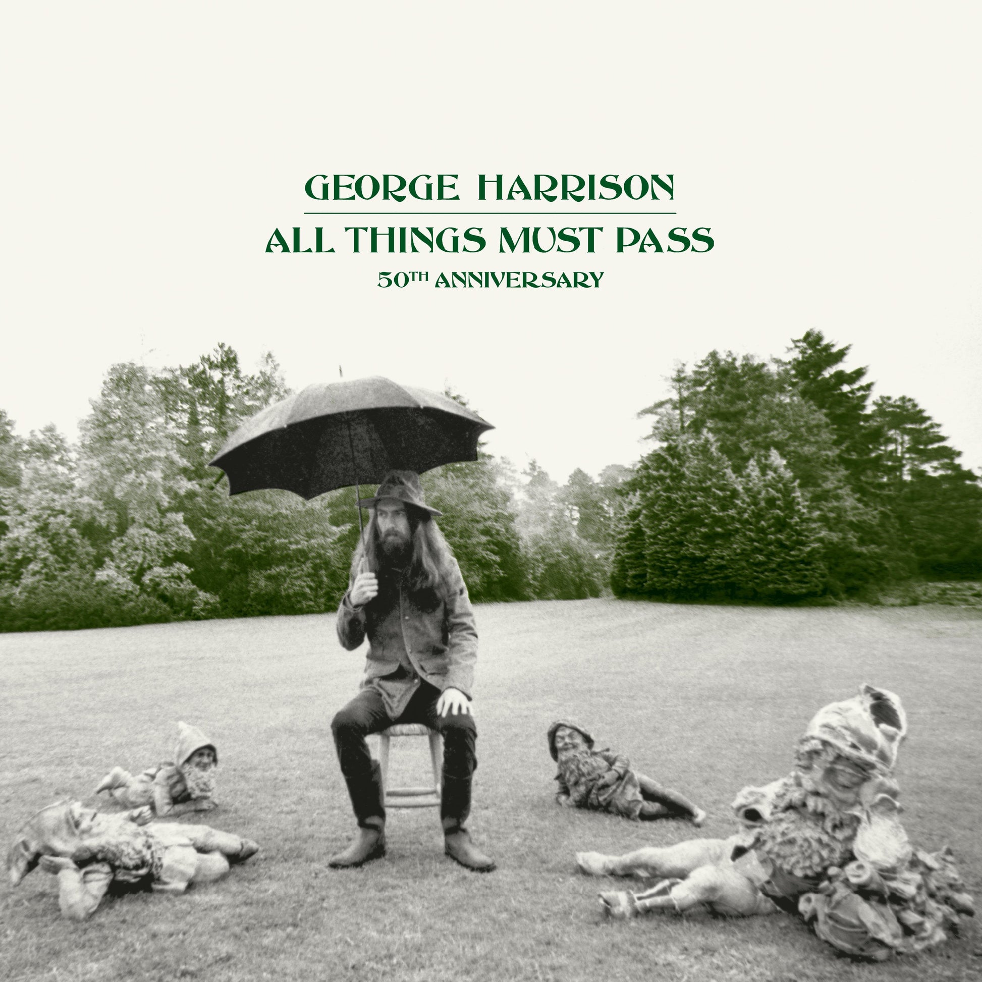 George Harrison sits on a stool under an umbrella surrounded by garden gnomes.