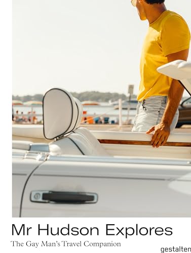 Man in yellow leans on a white boat near a beach.