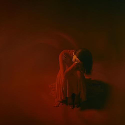 Woman in red dress, kneeling with head in hands, red lighting.