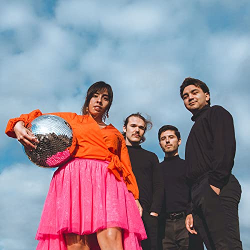 Four people posing against a cloudy blue sky, holding a disco ball.