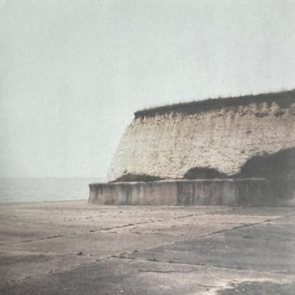 Black and white coastal cliff face with concrete structure foreground.