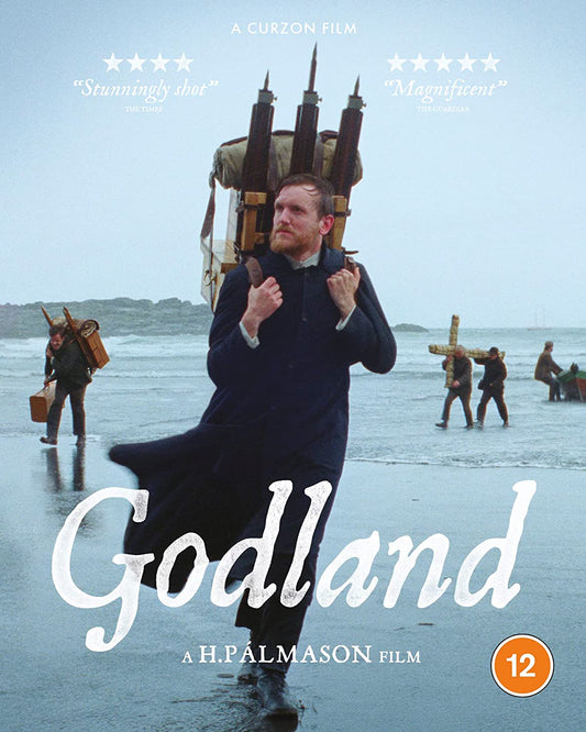 "Man in dark coat carrying artillery on beach with others in the background."