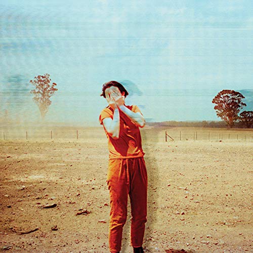 Woman in orange suit covering eyes in a dry, rural landscape.
