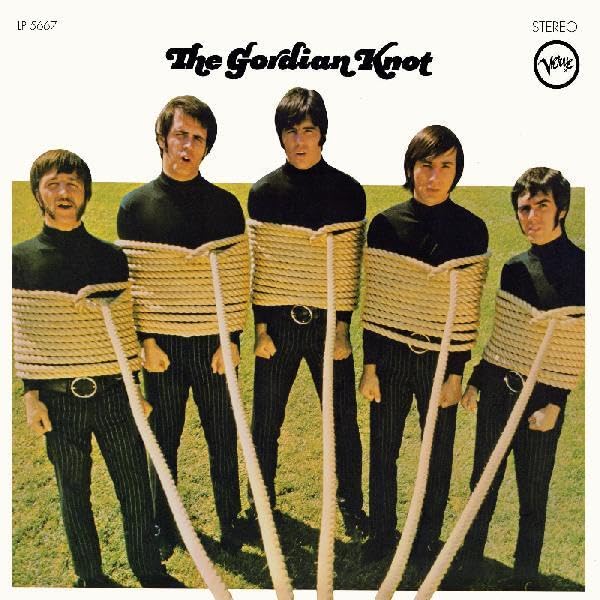 Album cover: four men tied with rope, standing in a field.