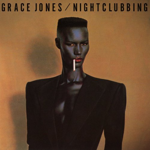 Grace Jones with a flat-top haircut and a cigarette against a tan background.