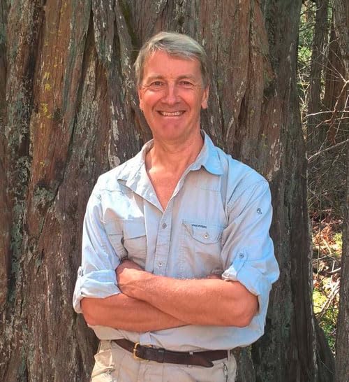 Portrait of a smiling man with gray hair, leaning against a tree.
