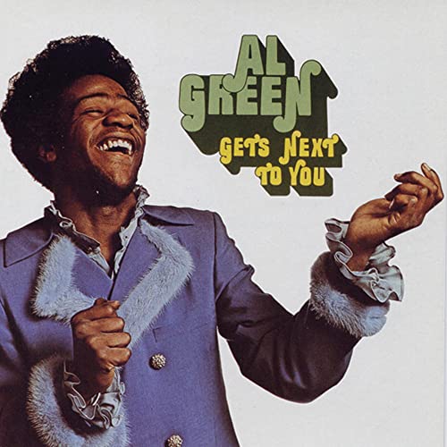 Al Green smiling, wearing a blue jacket with fur trim, on album cover art.