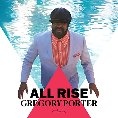 Gregory Porter in a suit stands before a pool and pink triangle.