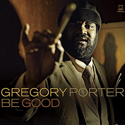 Gregory Porter wearing a hat and suit, gesturing with his hand in warm lighting.
