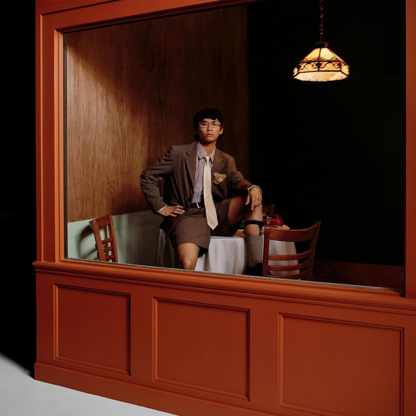 Young man in suit shorts sits in a restaurant window.