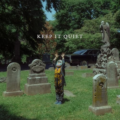 Person in patterned suit stands in a graveyard with a car.