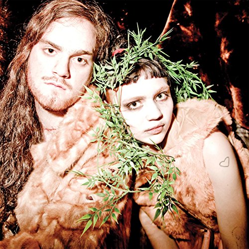A man and woman wearing faux fur, with green leaves framing the woman's face.