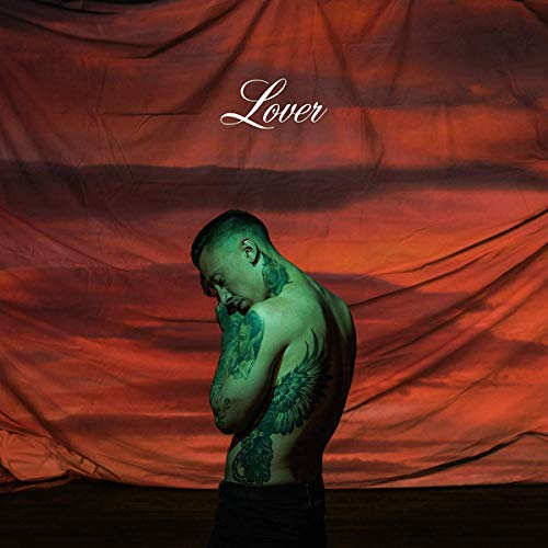 A shirtless tattooed man stands before a draped red fabric background with text Lover.