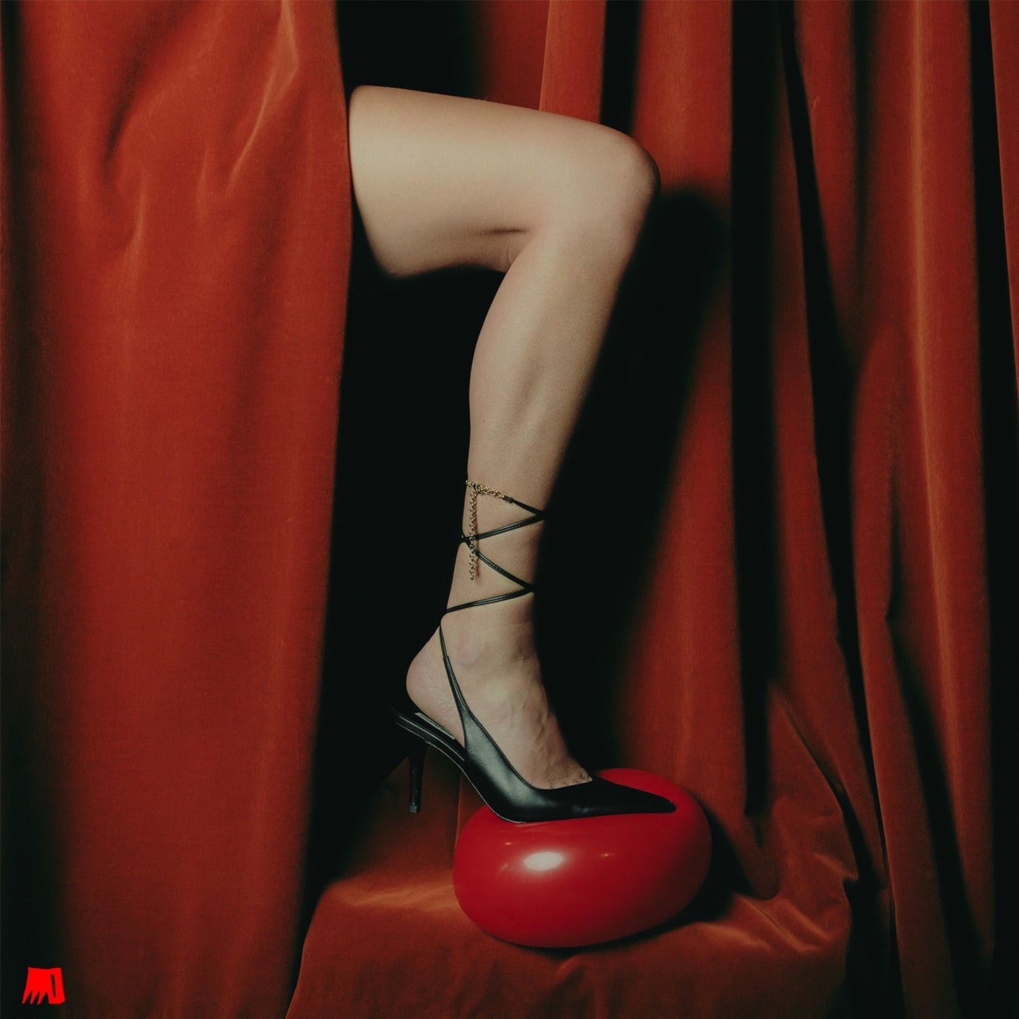 Person’s legs in black heels and ankle ties, red background.