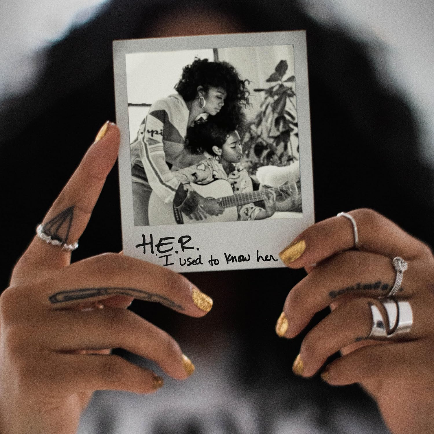 Hand holding a photo of H.E.R. playing guitar with a child.