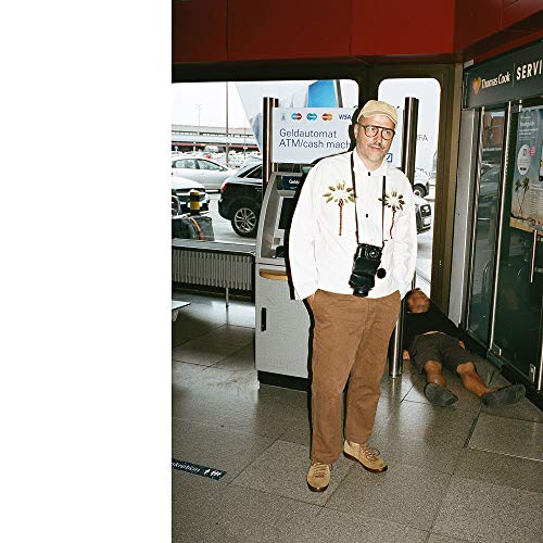 A man in a white shirt and brown pants stands in a train station.