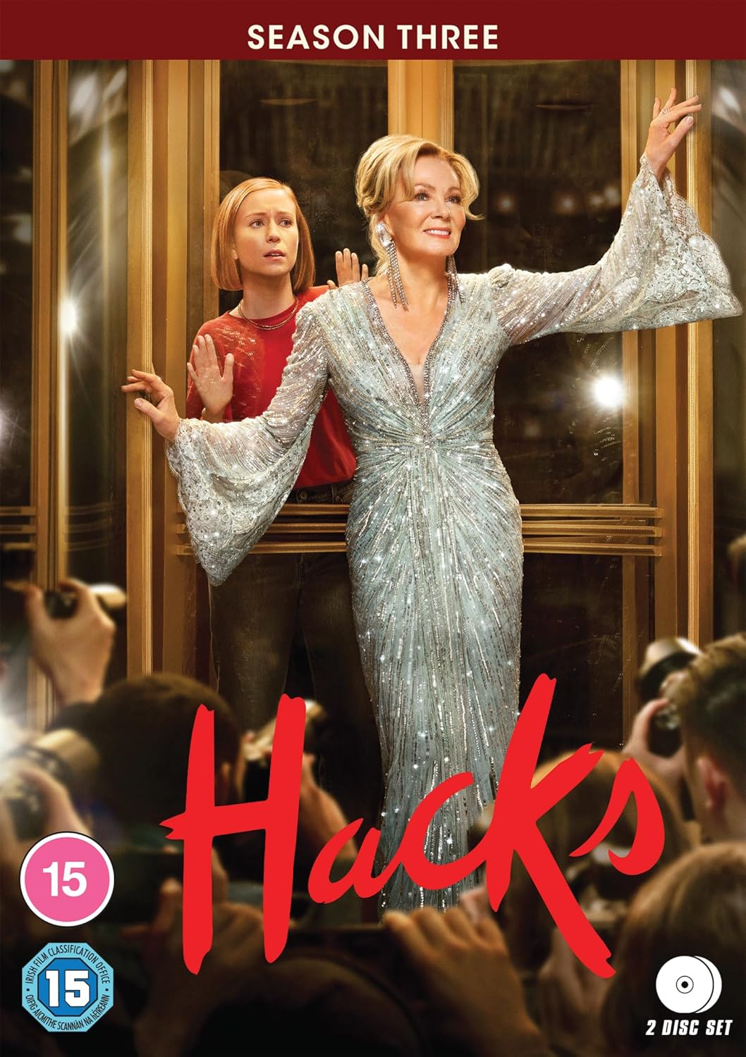 Two women stand in a doorway facing photographers, with the title Hacks in red.