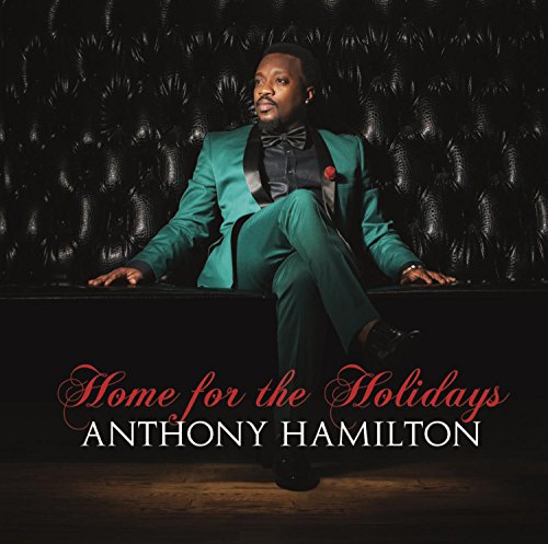 Anthony Hamilton in a green suit sits on a black leather couch.