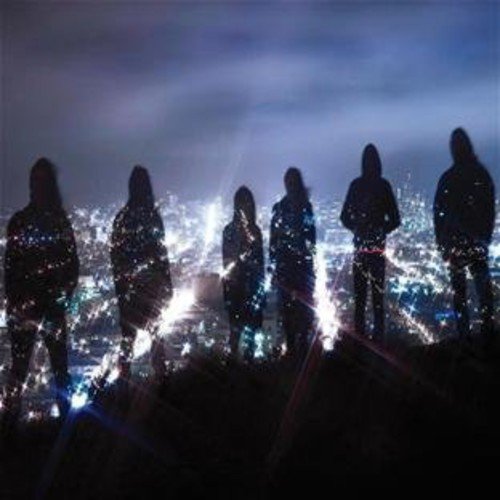 Silhouetted figures of five people stand on a hill overlooking a cityscape at dusk.