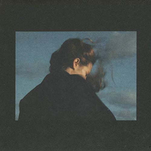 A person with windblown hair looks downward against a blue, cloudy sky.