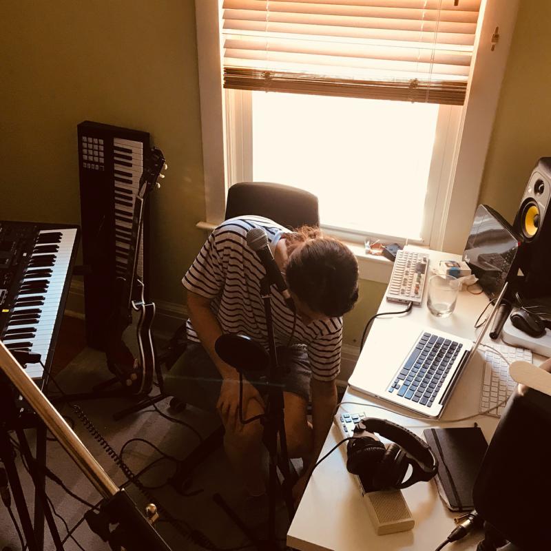 Woman with guitar recording music in a home studio setup.