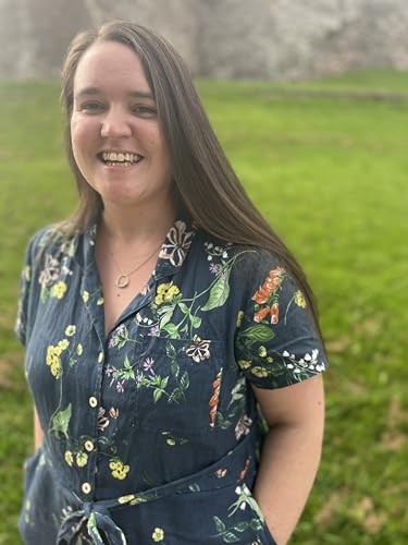 A smiling woman with long brown hair wearing a dark floral shirt outdoors.