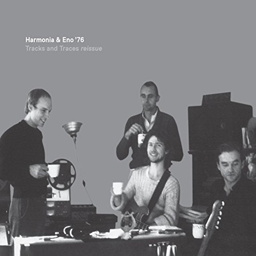 Four men in a studio setting with musical equipment and cups on a grey background.