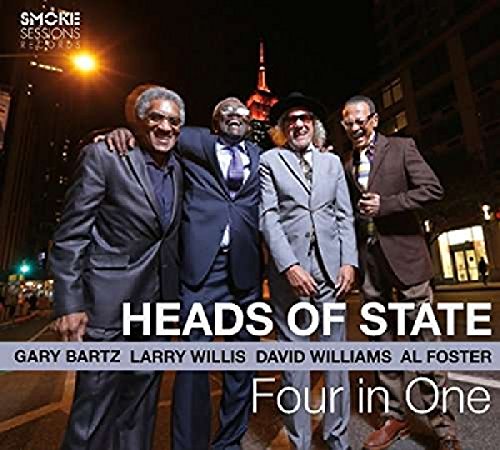 Four men in suits stand together on a city street at night.