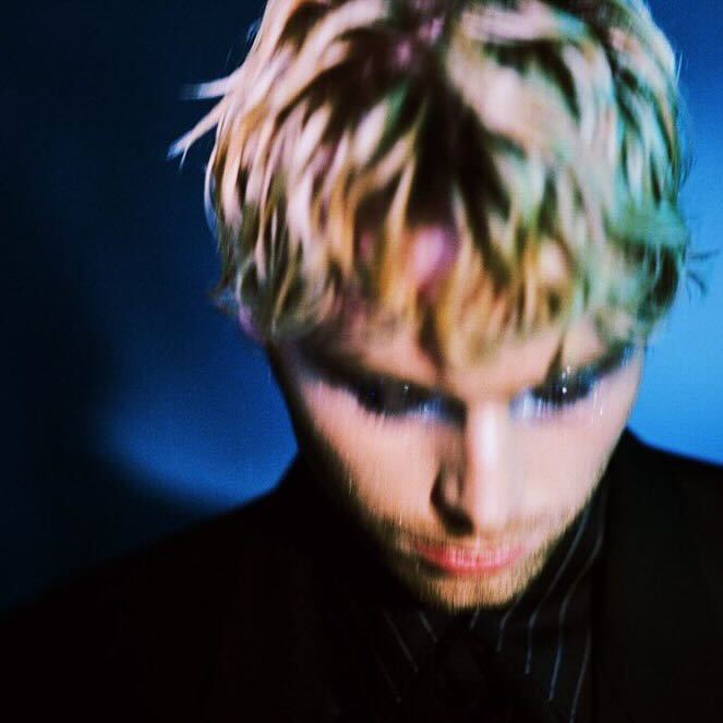 Close-up of a young man with blonde hair and dark eye makeup.