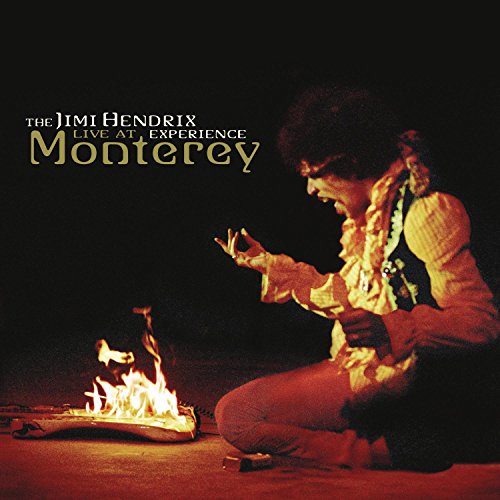 Jimi Hendrix kneeling, playing guitar beside a burning guitar onstage.