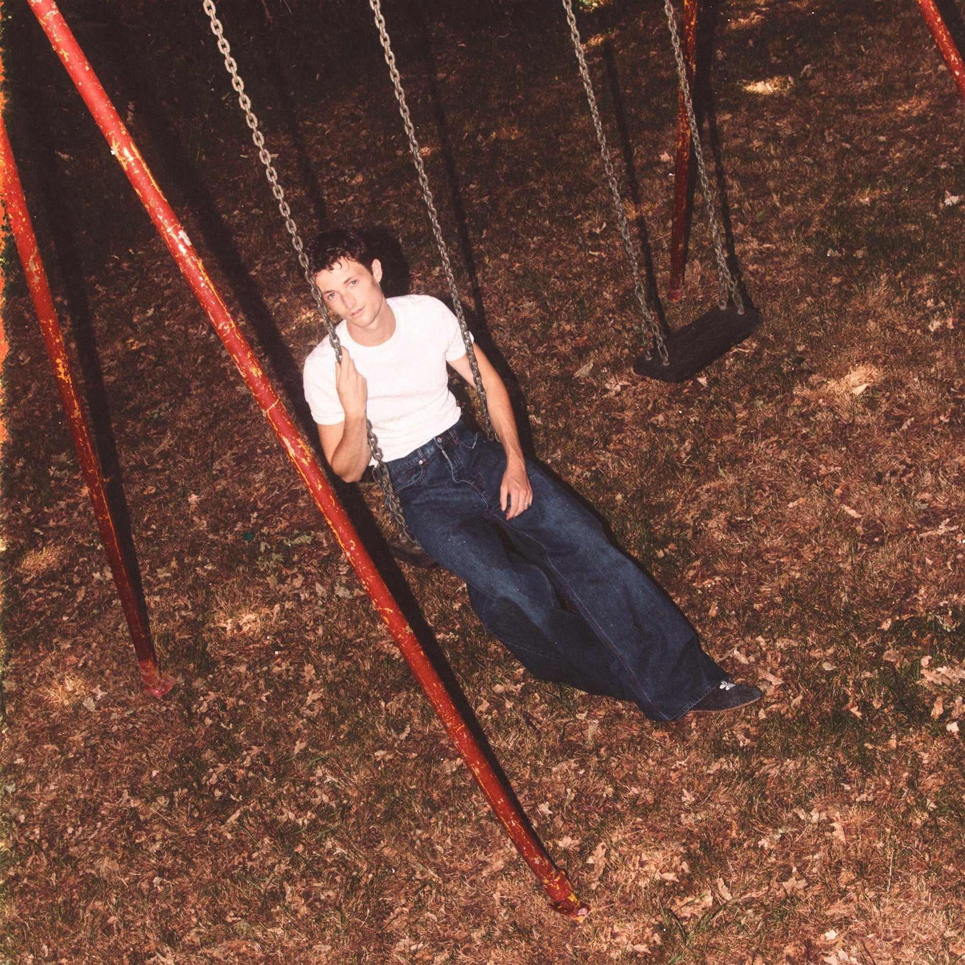 Young man in a white shirt lying on a swing set.