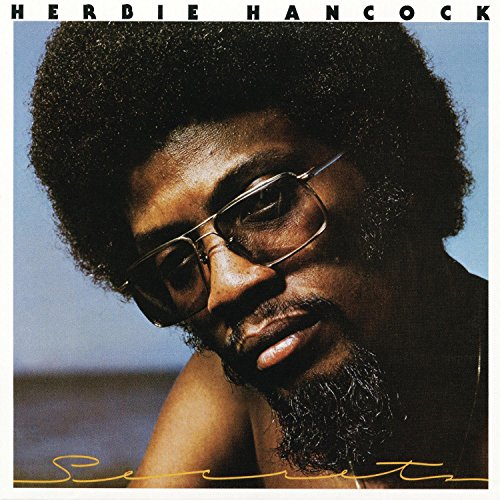 Close-up portrait of Herbie Hancock wearing glasses against a blue sky background.