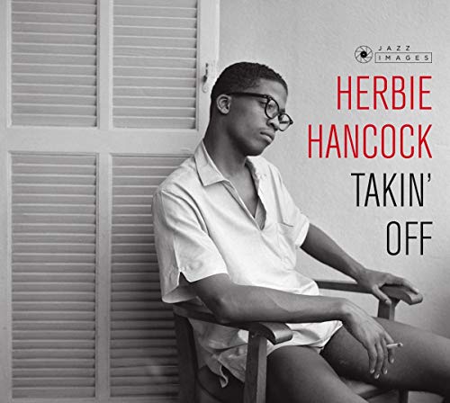 Black and white portrait of Herbie Hancock wearing glasses, sitting in a wooden chair.