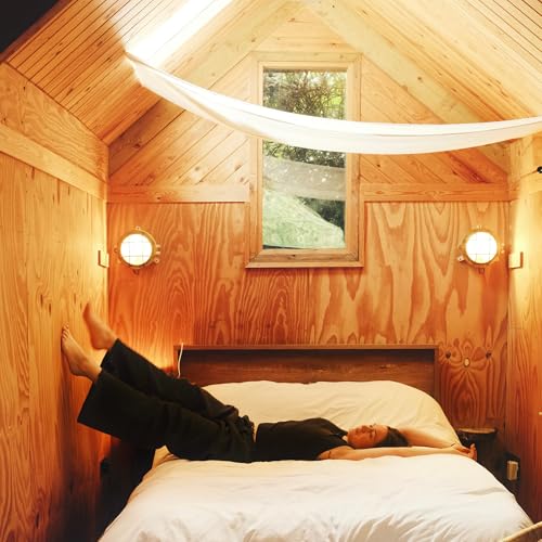 Person lying on a bed inside a small, wooden-walled room.