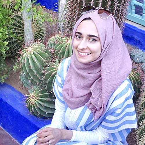 Young woman wearing a hijab and sunglasses smiles at the camera.