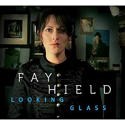 Fay Hield in a dark military-style jacket against a dimly lit room background.