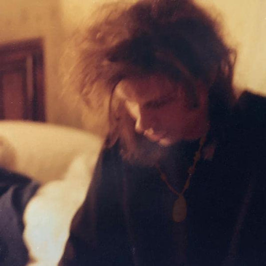 A person with messy hair looks downward in a dimly lit, warm-toned indoor setting.