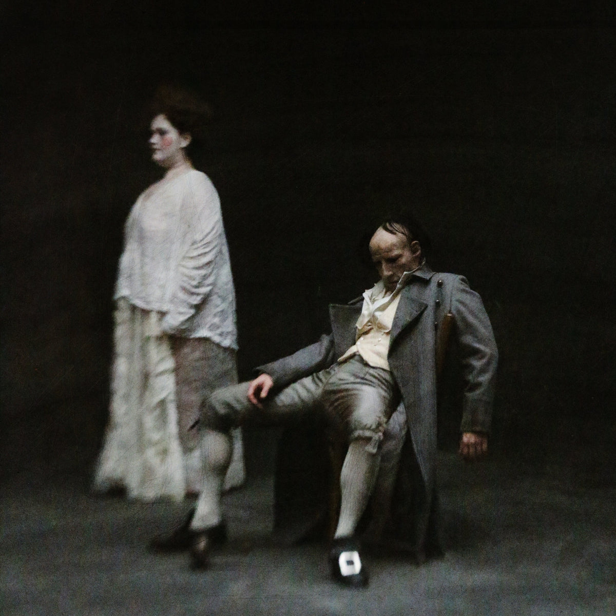 Two figures in vintage clothing, blurred, against a dark background.