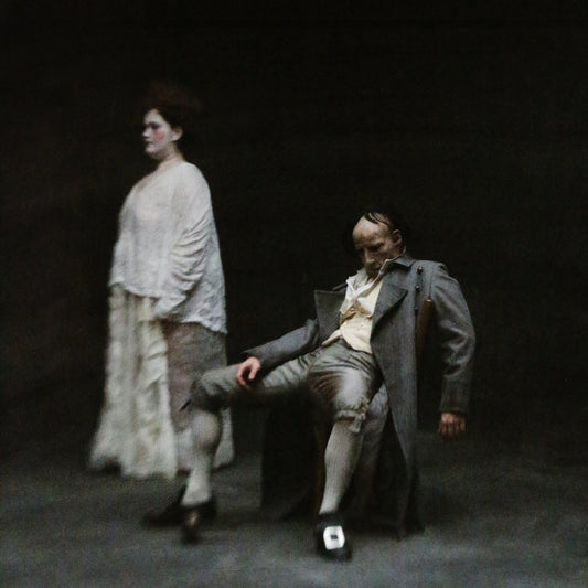 Two figures in vintage clothing, blurred, against a dark background.