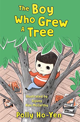 Boy sits in a tree with green leaves over a wooden floor.