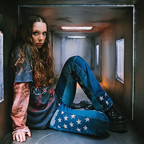 A woman with long wavy hair sits inside a narrow, dimly lit rectangular corridor.