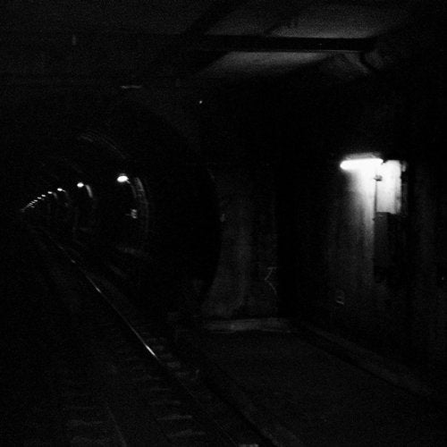 A dark, black and white view of a train tunnel with dim wall lights.