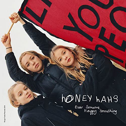 Three women in black puffer jackets posing under a red banner with black text.