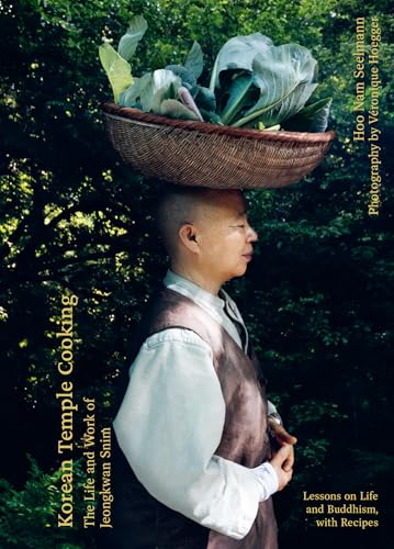 A Buddhist nun balances a woven basket of leafy greens on her head outdoors.