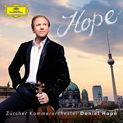 Man in a tuxedo holding a violin with a cityscape and cloudy sky background.