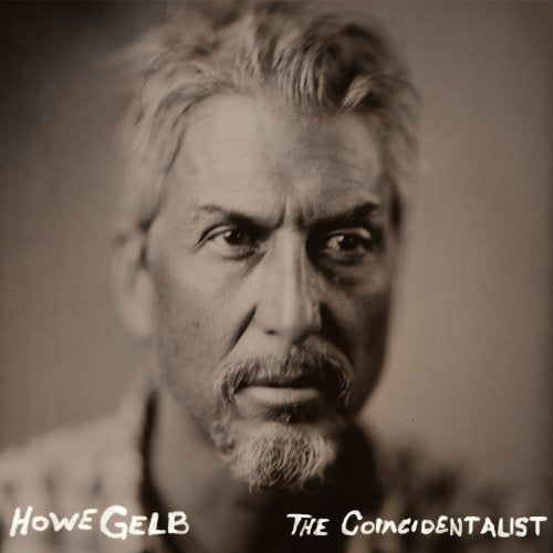 The image is a black-and-white album cover featuring a close-up portrait of a man with a serious expression. The man has short, light-colored hair and a goatee, and is looking directly at the camera. The background is blurred, but appears to be a plain wall or other neutral surface. * The man's face is the main focus of the image, taking up most of the space. * He has a serious expression on his face, with a furrowed brow and a