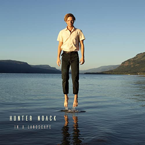 Man levitating above water with mountains in the background.