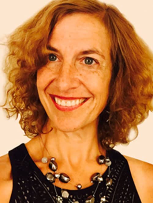 Woman with curly brown hair smiling, wearing a beaded necklace.