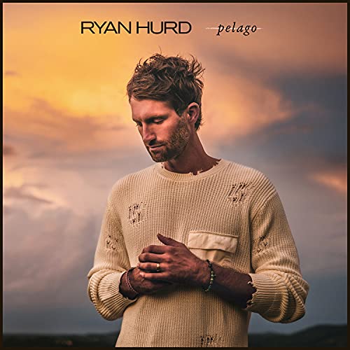 Ryan Hurd wearing a distressed cream sweater against a sunset sky background.